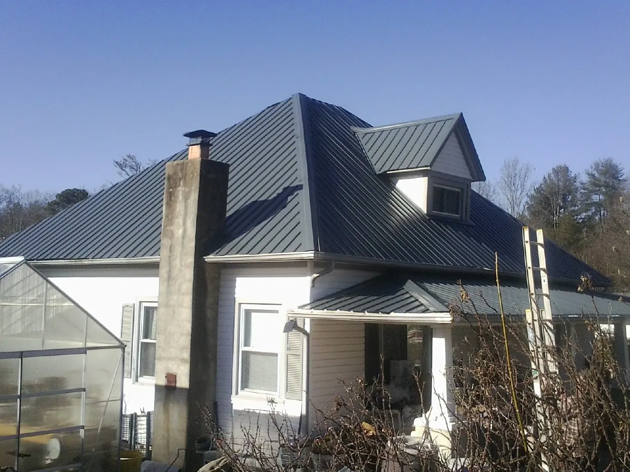 Dark blue standing seam metal roof on a white farmhouse with dormer — Slate & Tile Roof Repair by Roofing Brothers in Gracemont