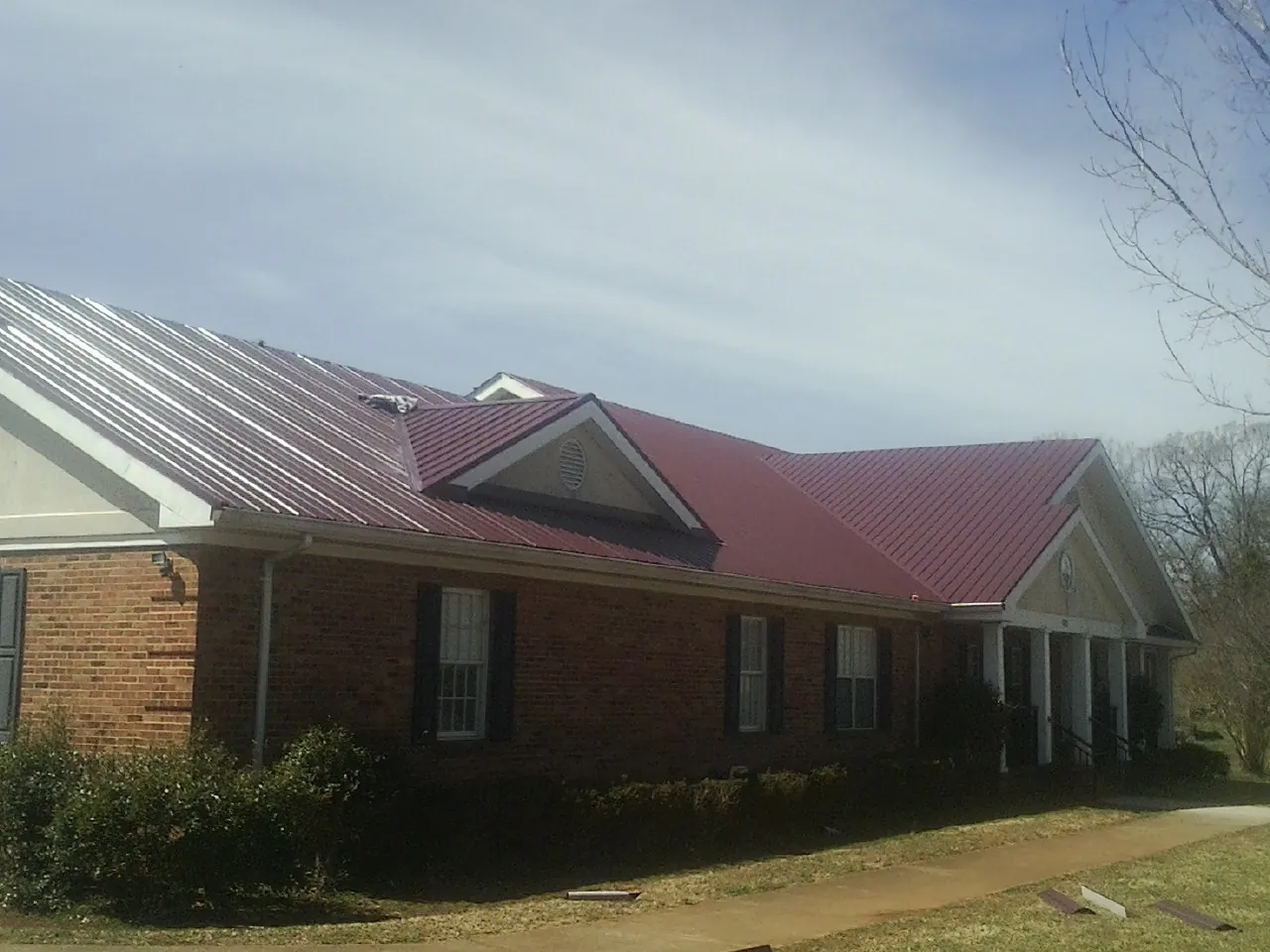 Red metal roof with gabled entries on a long brick building, from a Hail Damage Roof Repair job in Gracemont