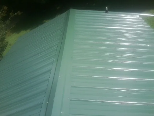 New green metal panels meeting at the ridge of a roof — Flat Roof Repair work by our crew in Gracemont