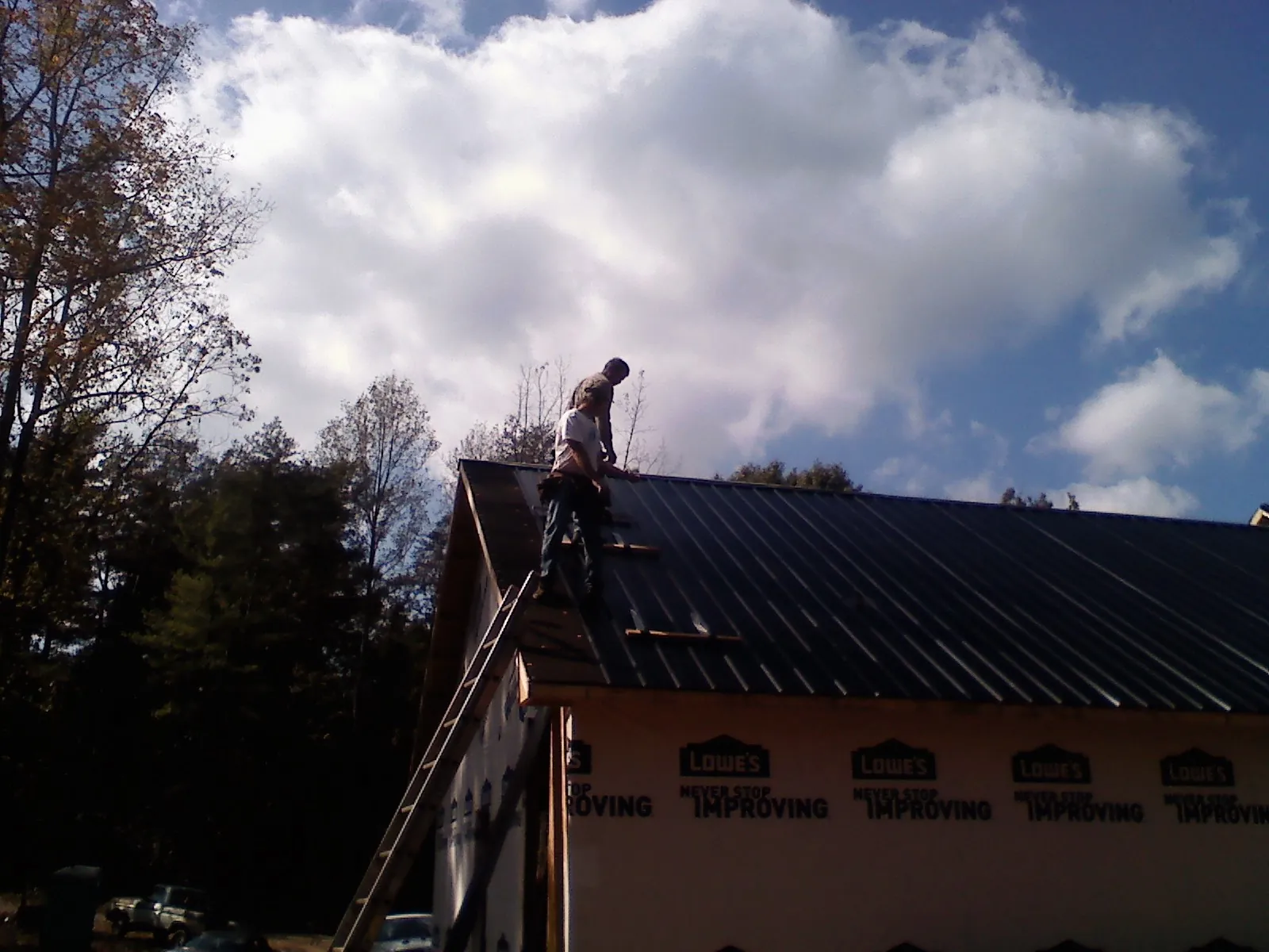 Roofer fastening dark metal panels high against a cloudy sky, from a Roof Inspection job in Gracemont