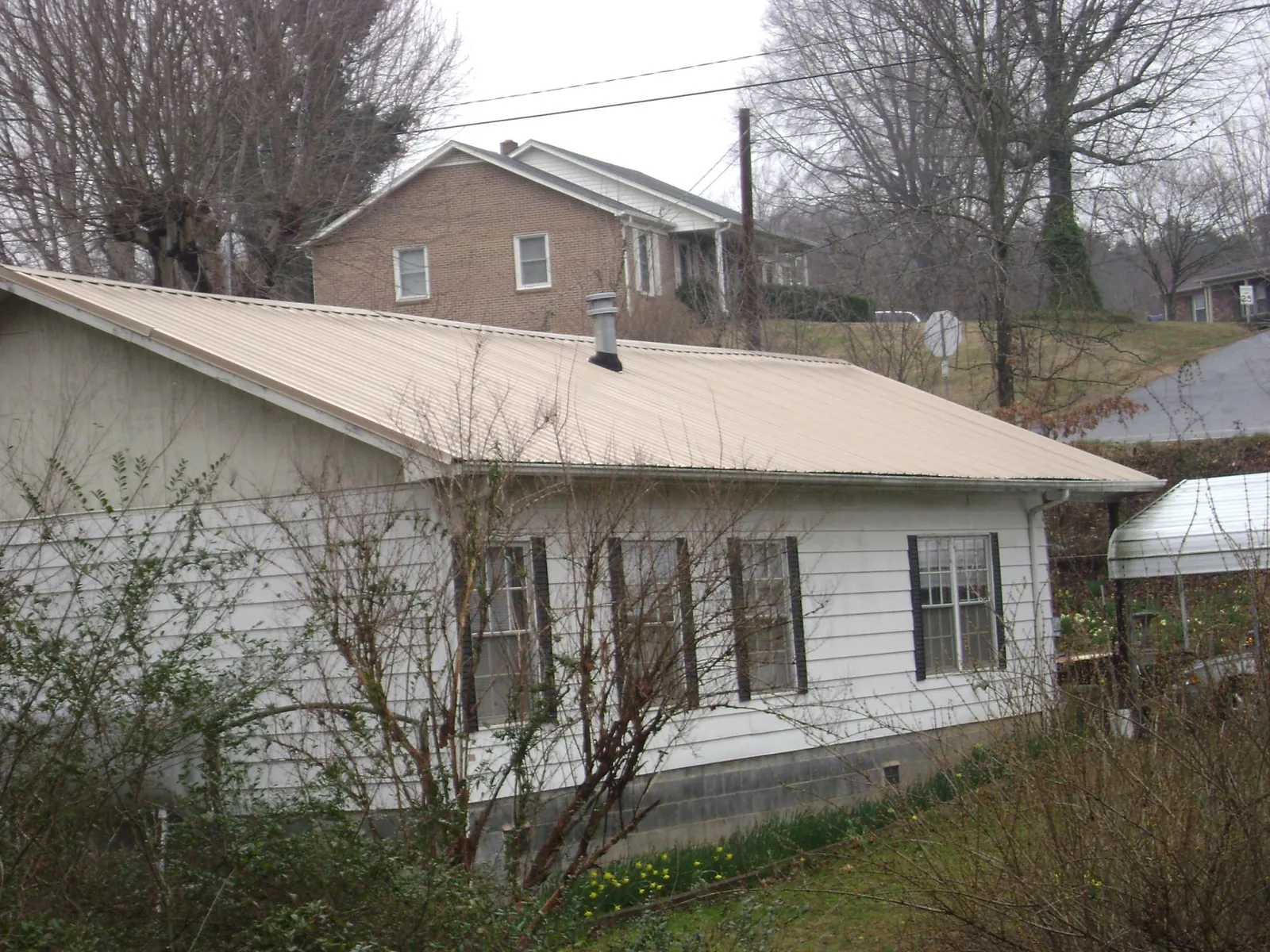 Tan metal roof on a white sided house set into a hillside — Commercial Roofing by Roofing Brothers in Gracemont