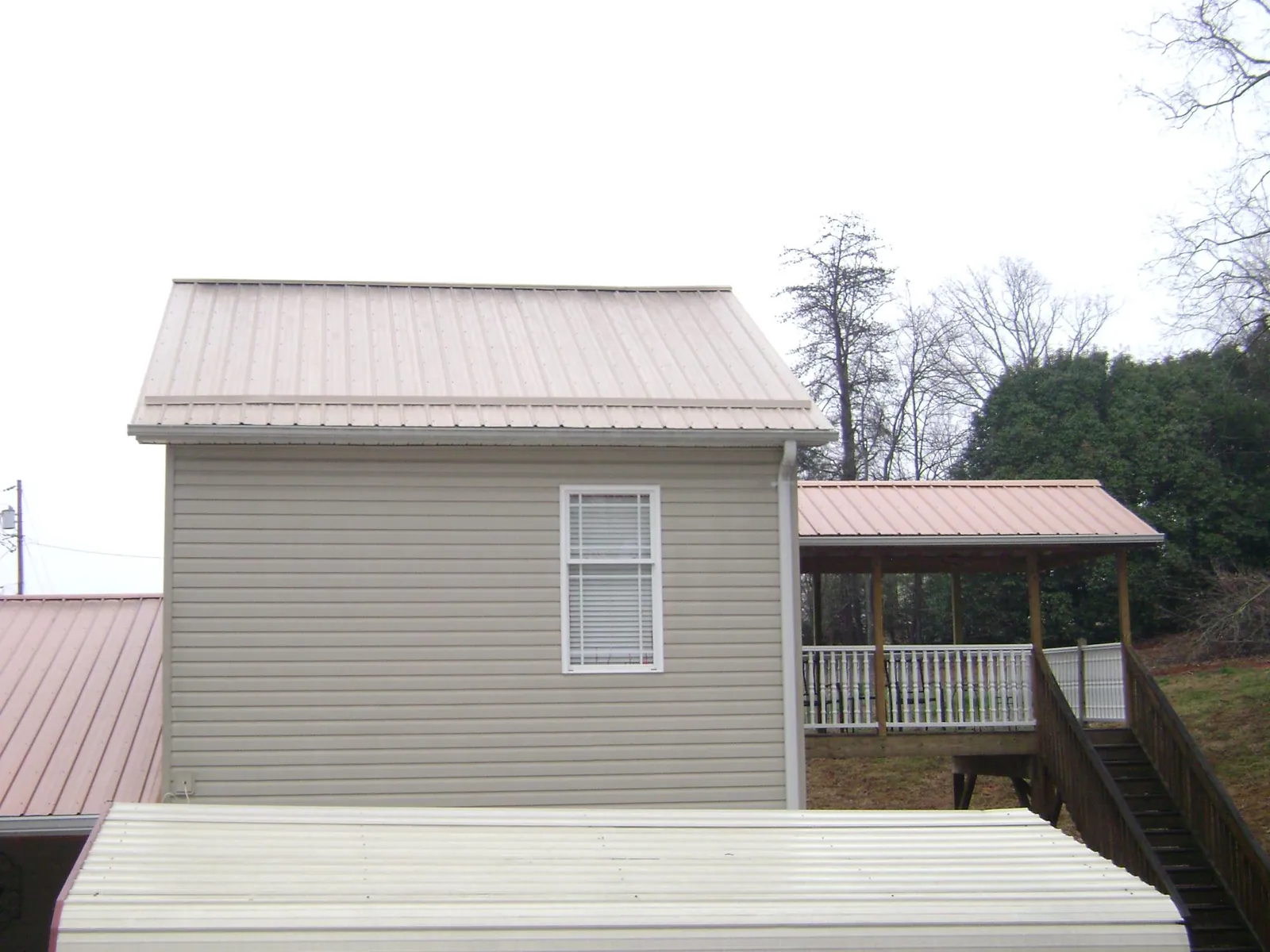 Tan metal roofs on a two story addition and attached porch, from a Roof Replacement job in Gracemont